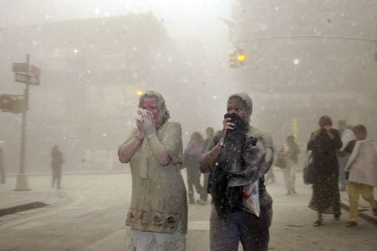 In this Sept. 11, 2001 photo, people covered in dust from the collapsed World Trade Center buildings, walk through the area, in New York. Two decades after the twin towers