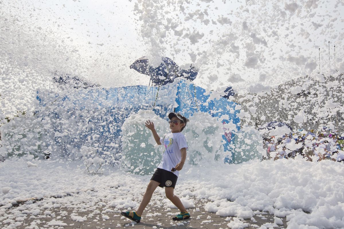 A child walks past machines blowing out foam during the Bubble Show event in Beijing, China, Sunday, June 26, 2016. Thousands of residents enjoy colored foam churned out by machines along a running track at the event designed for children and parents’ interaction. (Ng Han Guan / Associated Press)