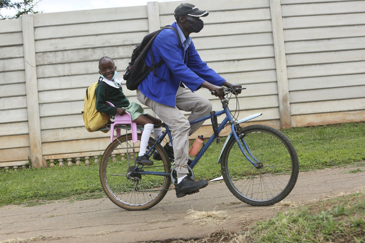 A parent transports his child to school using a bicycle in Harare, Zimbabwe, Wednesday, Feb, 9, 2022. A pay strike by teachers has paralyzed learning at many Zimbabwean schools, which belatedly opened on Monday after a pandemic-induced prolonged closure. (Tsvangirayi Mukwazhi)