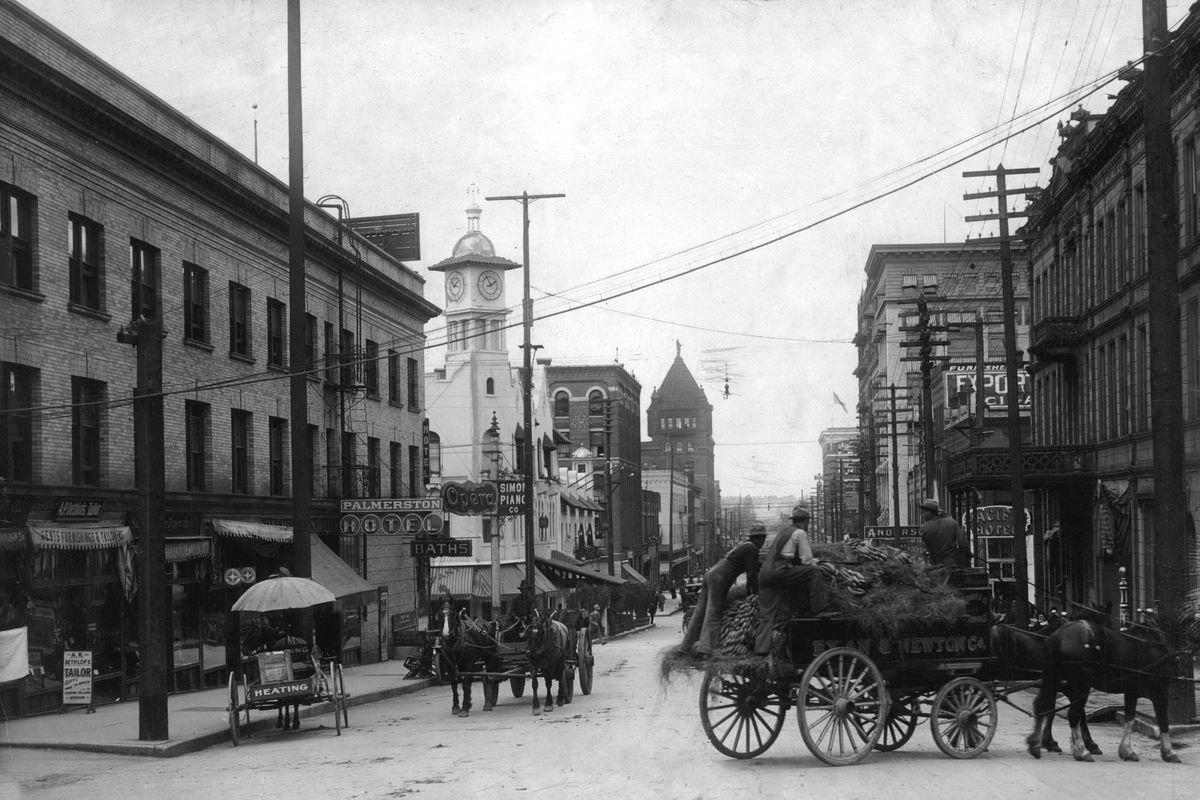 Circa 1906 - Looking north down Post Street, the white building at center left, with the clock in its ornate tower, the three-story Pennington Hotel at the corner of First Avenue and Post Street. The hotel is attached to Louis Davenport’s two-story restaurant. In the foreground, a wagon from Ryan and Newton Co., a livery stable operator, hauls hay and feed. Davenport was vice president of Ryan and Newton and part of several major businesses. (SPOKESMAN-REVIEW PHOTO ARCHIVE / SR)