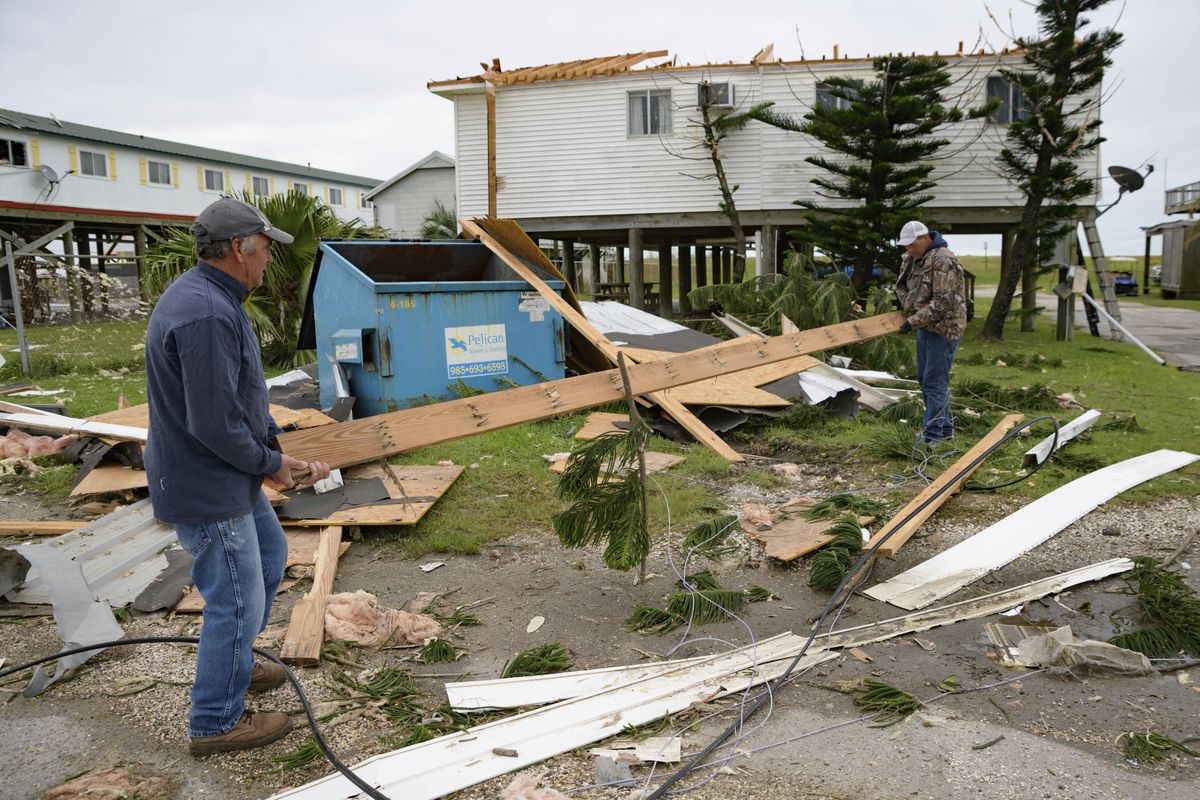 Mark Andollina, left, and Shane Holder, remove part of a roof damaged by Hurricane Zeta on Friday from the road at the Cajun Tide Beach Resort in Grand Isle, La. (Matthew Hinton)