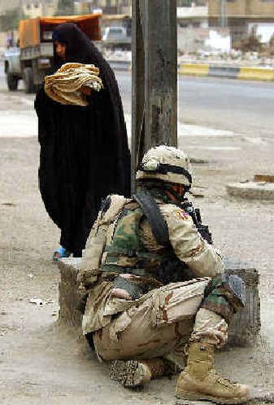 
An Iraqi woman passes a U.S. soldier taking cover after troops came under fire in Baghdad on Wednesday after a car bomb rammed into a civilian convoy, setting vehicles on fire.
 (Associated Press / The Spokesman-Review)