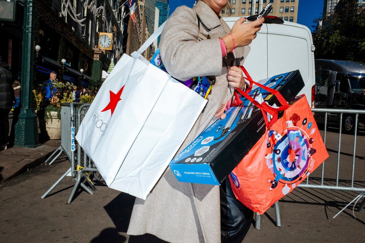 Laden with packages, a shopper checks her phone while crossing a street outside the flagship Macy’s store in midtown Manhattan last Saturday.  (New York Times)
