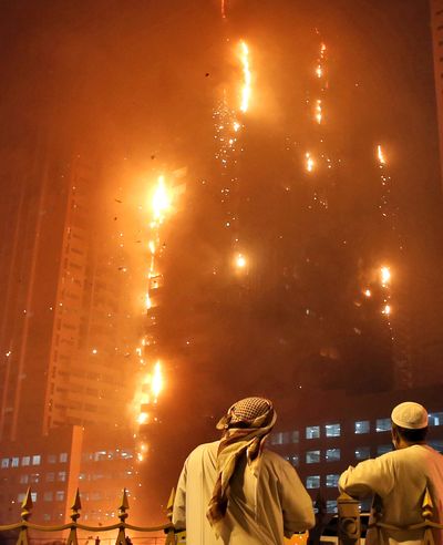 Two Emirati officials watch as a fire spreads up the side of a high-rise building in Ajman, United Arab Emirates, early Tuesday. (Kamran Jebreili / Associated Press)