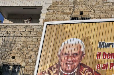 A Palestinian woman in the West Bank town of Bethlehem stands next to a rotating banner showing Pope Benedict XVI. The pope will visit Israel and the West Bank during a five-day tour.  (Associated Press / The Spokesman-Review)