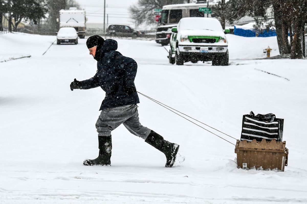 Ronald DeVine, 30, dashes through the snow with a two-container setup to haul his groceries as he makes his way along 5th Avenue at Regal Street during the morning snowfall, Dec. 20, 2021 in Spokane. DeVine had just left the nearby Fred Meyer and drug the bins about a half mile. He said waxing the bottom helped.  (DAN PELLE/THE SPOKESMAN-REVIEW)