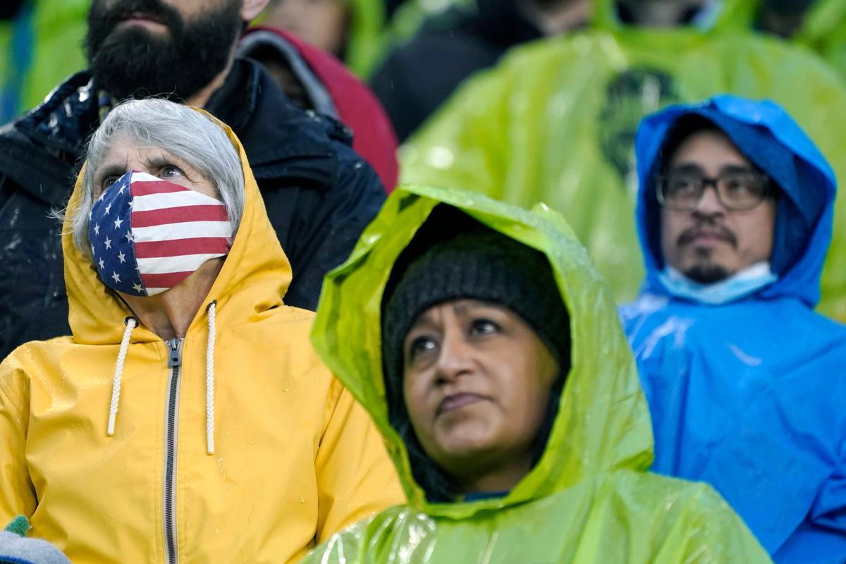 FILE - A person wears a U.S. flag face mask during the national anthem before an MLS soccer match between the Seattle Sounders and Nashville SC, Feb. 27, 2022, in Seattle. Many Americans are significantly relaxing how often they wear masks and take other once-routine precautions against the coronavirus. A new poll from The Associated Press-NORC Center for Public Affairs Research shows fewer than half now say they regularly wear face masks, avoid crowds and skip nonessential travel. Americans are letting their guard down as new COVID-19 infections plummet to their lowest level since July.  (Ted S. Warren)