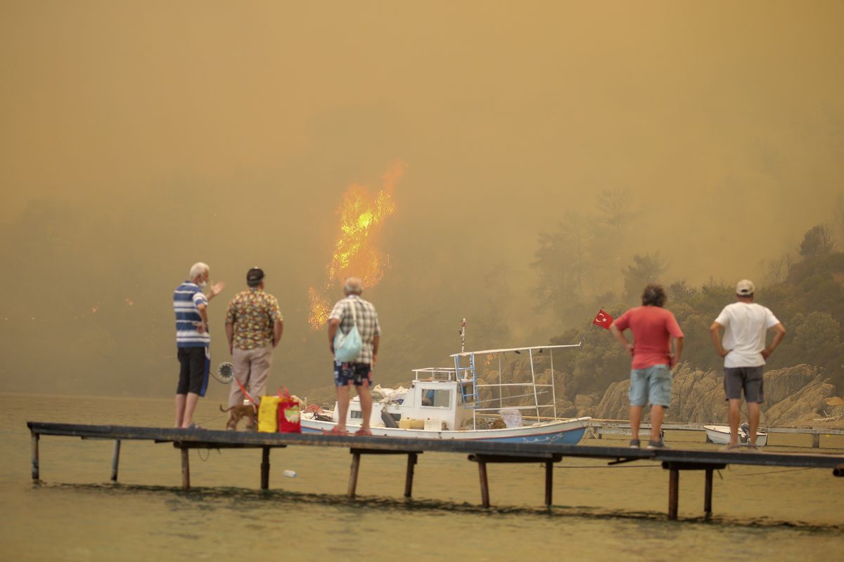 Tourists wait to be evacuated from smoke-engulfed Mazi area as wildfires rolled down the hill toward the seashore, in Bodrum, Mugla, Turkey, Sunday, Aug. 1, 2021. More than 100 wildfires have been brought under control in Turkey, according to officials. The forestry minister tweeted that five fires are continuing in the tourist destinations of Antalya and Mugla.  (Emre Tazegul)