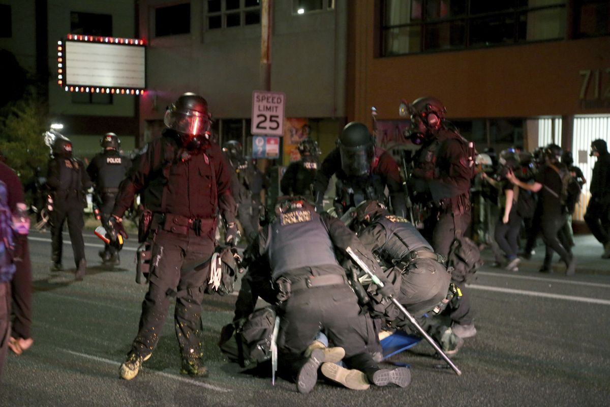 Portland police declare a riot at the Multnomah County Building, on Tuesday, Aug. 18, 2020, in Portland, Ore. Officers made at least two arrests of protesters. Officials say protesters in Portland broke out the windows of a county government building, sprayed lighter fluid inside and set it on fire in a demonstration that ended with clashes with police.  (Beth Nakamura)