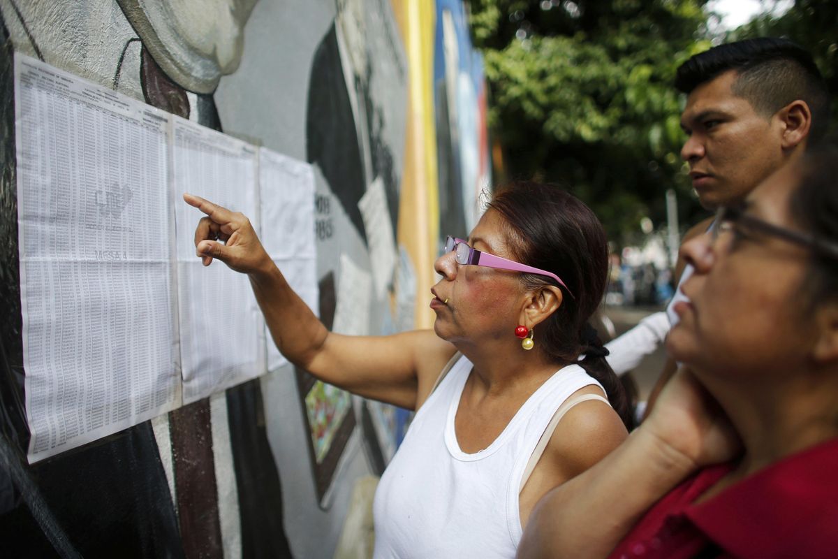 People check their voting machine at a list of voters provided by Venezuelan National Electoral Council, CNE, outside of a poll station during the election for a constitutional assembly in Caracas, Venezuela, Sunday, July 30, 2017. The run-up to Sunday’s vote has been marked by months of clashes between protesters and the government. (Ariana Cubillos / Associated Press)