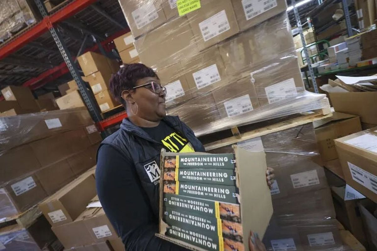 Joleen Simmons, managing supervisor at the Harbor Island warehouse for Mountaineers Books, carries a stack of the 10th edition of “Mountaineering: The Freedom of the Hills” through the warehouse earlier this month.  (Ivy Ceballo/The Seattle Times)