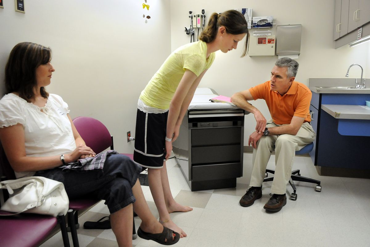 Dr. Paul Caskey, chief of staff and orthopedic surgeon at Shriners Hospital for Children in Spokane, checks the range of movement in Samantha Viehouser’s back during a post-surgery checkup. Samantha has about $20,000 worth of titanium rods and screws in her back to correct scoliosis. Shriners Hospital is now billing insurance companies for the cost of the care. Samantha’s mother, Lynett, is at left. (Dan Pelle)