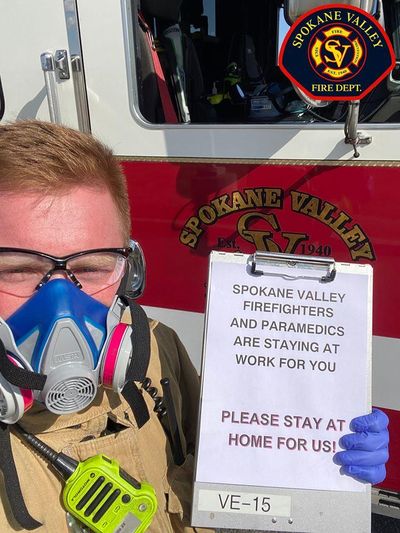 In this courtesy image from March 20, 2020, a Spokane Valley firefighter carries a message urging residents to remain home to stop the spread of the coronavirus. Dispatchers are asking additional questions during medical calls to ensure patients and firefighters are safe amid orders to keep your distance from others. (Spokane Valley Fire Department / Courtesy)