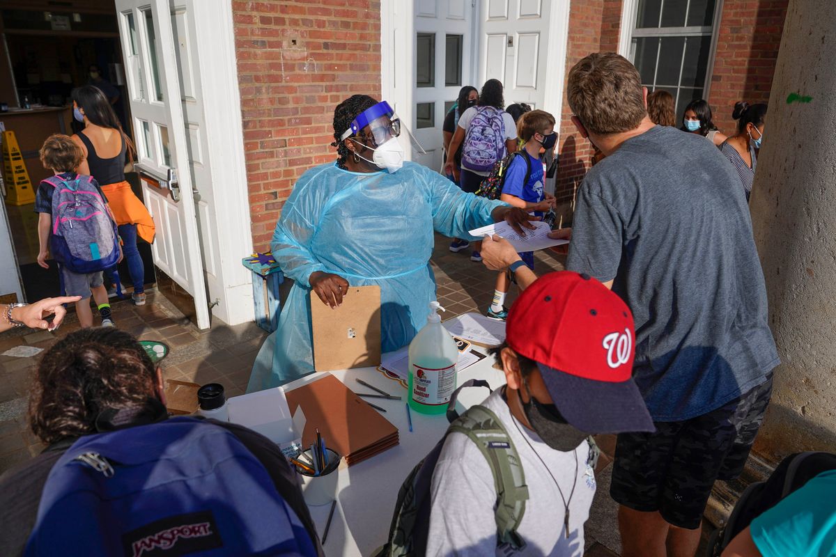 FILE — A Healthcare worker directs parents and students arriving at the main entrance of the Adams campus of Oyster-Adams Adams bilingual school, in Washington, Aug. 30, 2021. The District of Columbia on Dec. 22, 2021, said all students, whether in public, private or charter schools, must be fully vaccinated by March 1, 2022.  (Pablo Martinez Monsivais)