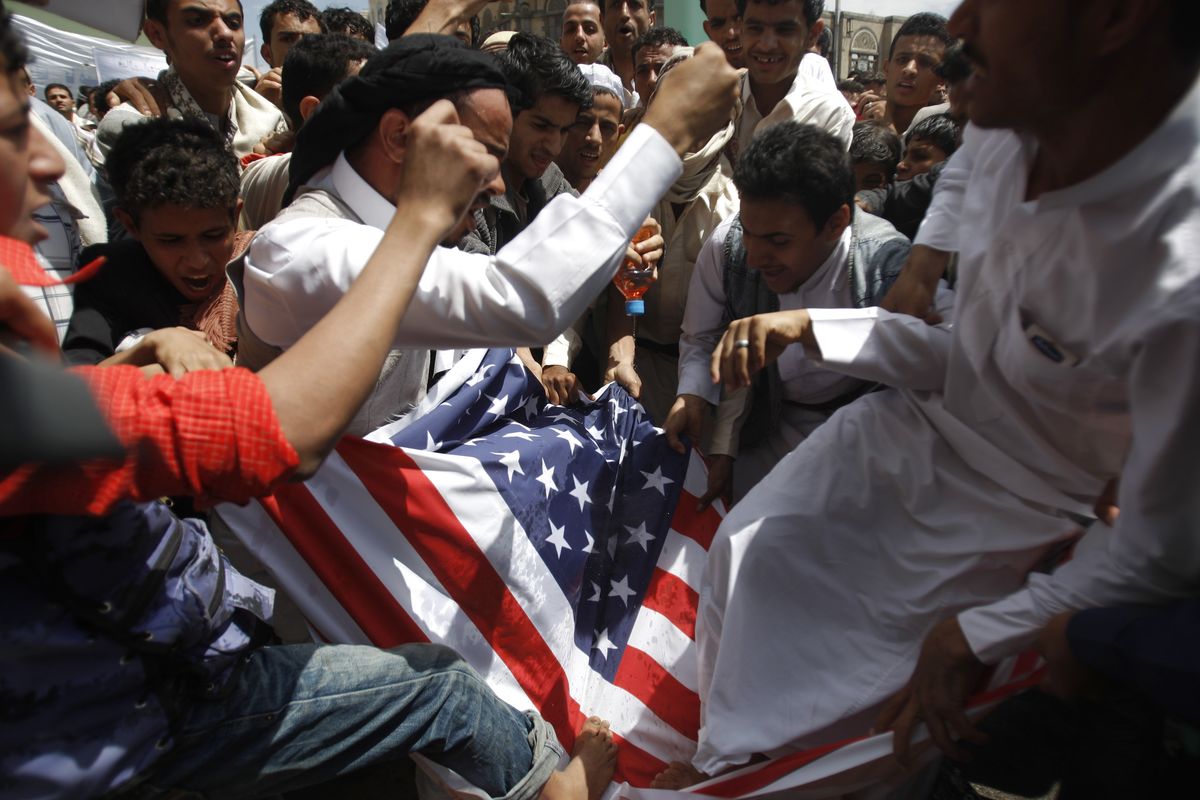 Protesters destroy an American flag pulled down during clashes with police near the U.S. Embassy in Sanaa, Yemen, on Friday. (Associated Press)