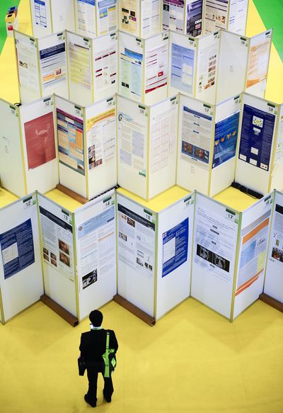 A visitor checks his mobile phone in front of posters during the European breast cancer conference in Barcelona, Spain, on Thursday.  (Associated Press)