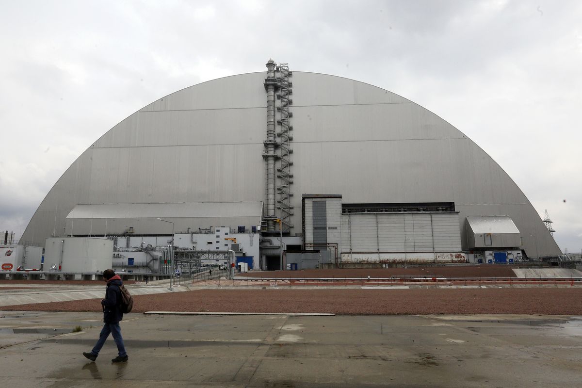 A man walks past a shelter covering the exploded reactor at the Chernobyl nuclear plant, in Chernobyl, Ukraine, Thursday, April 15, 2021. The vast and empty Chernobyl Exclusion Zone around the site of the world’s worst nuclear accident is a baleful monument to human mistakes. Yet 35 years after a power plant reactor exploded, Ukrainians also look to it for inspiration, solace and income.  (Efrem Lukatsky)