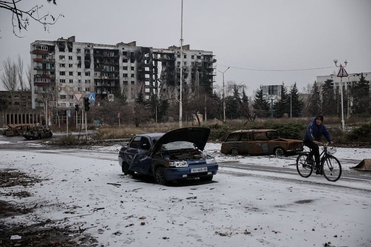 A resident rides a bicycle near apartment buildings and cars damaged by a Russian military strike, amid Russia