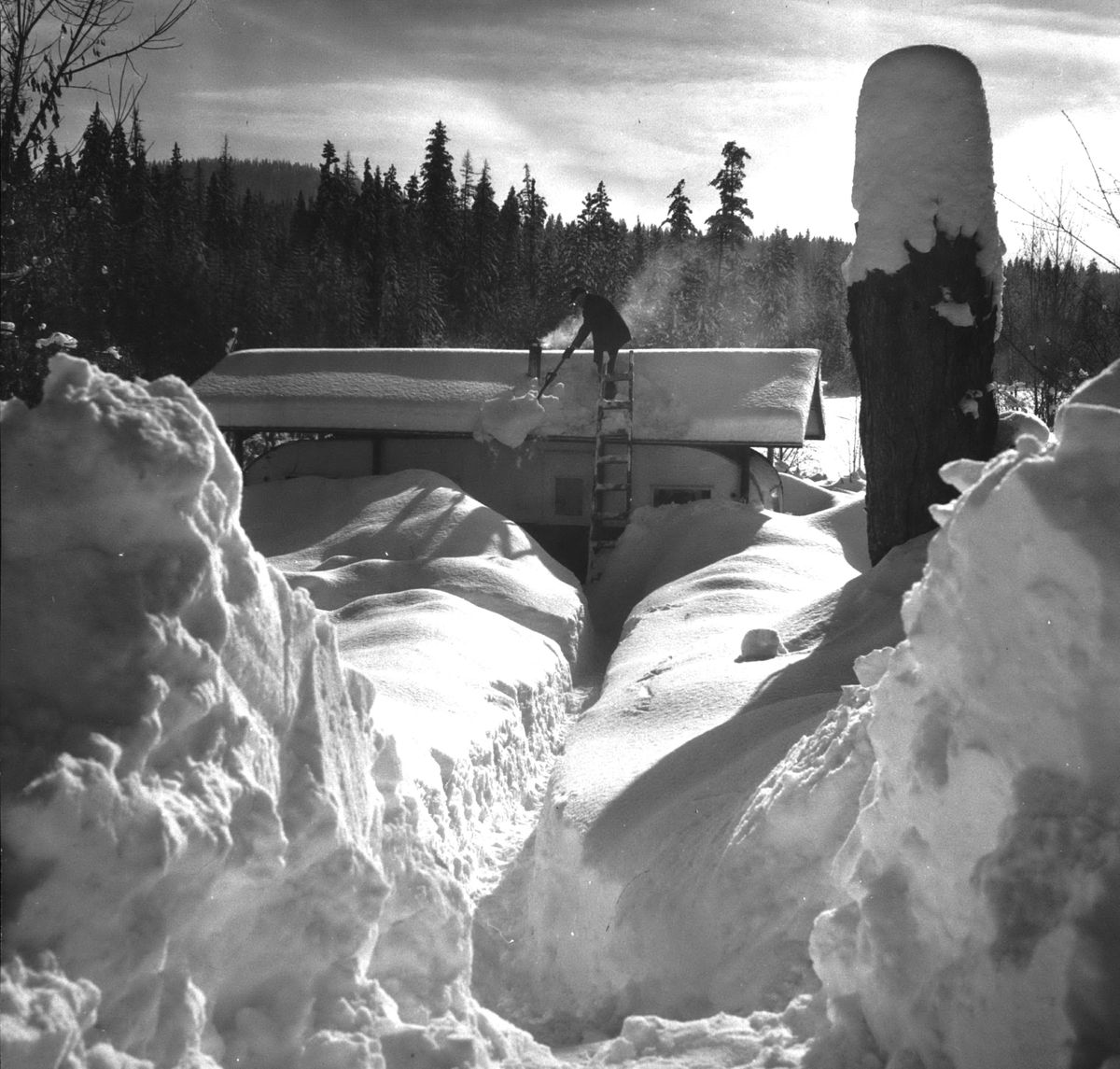 A man shovels snow off a roof covering a camper trailer surrounded by snow in 1969. (PHOTO ARCHIVE / SR)