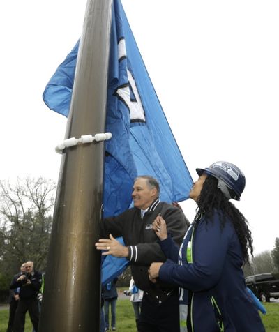 Washington Gov. Jay Inslee, left, and his executive assistant Angie Adams, right, raise the Seattle Seahawks 12th man flag, Thursday, Jan. 7, 2016, at the Capitol in Olympia, Wash. (AP Photo/Ted S. Warren)