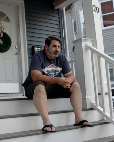 Davi Pedro sits on his porch in his Everett, Mass., neighborhood on July 28. An owner-operator, he recently sold his semi-truck because of the freight recession.  (Cassandra Klos/For the Washington Post)