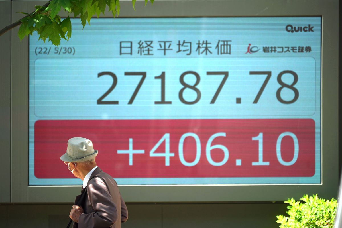 A man wearing a protective mask walks past an electronic stock board showing Japan