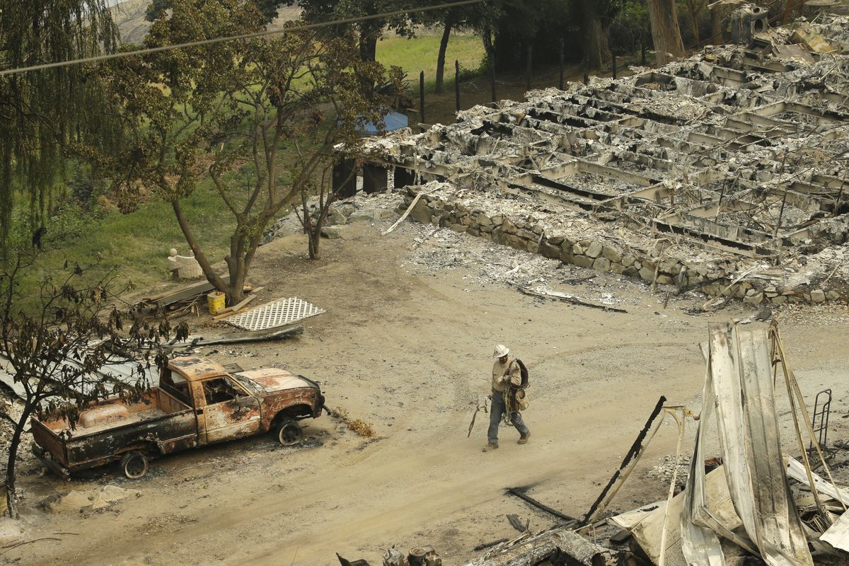 A Chelan County Public Utility District worker walks past a burned structure along state Route Alternate 97 highway Monday, outside of Chelan, Wash. (Associated Press)