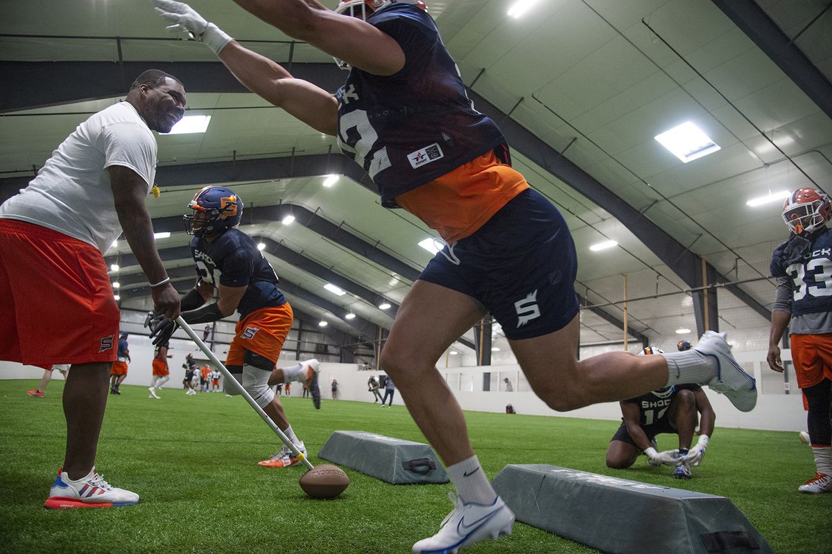 Spokane Shock Defensive Line Coach Qasim Mitchell, left, uses a ball on a pole to signal his players to move off the line during practice Monday, May 3, 2021 at an indoor practice facility in North Idaho.  (Jesse Tinsley/The Spokesman-Review)