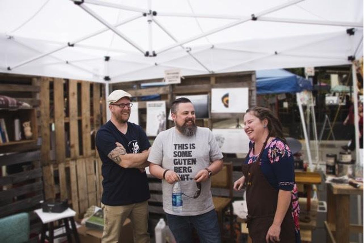 Thom Caraway, Derek Landers and Bethany Taylor hang out at the Millwood Print Works booth at Bazaar in downtown Spokane on Saturday, June 17. (Daniel DC Parker)