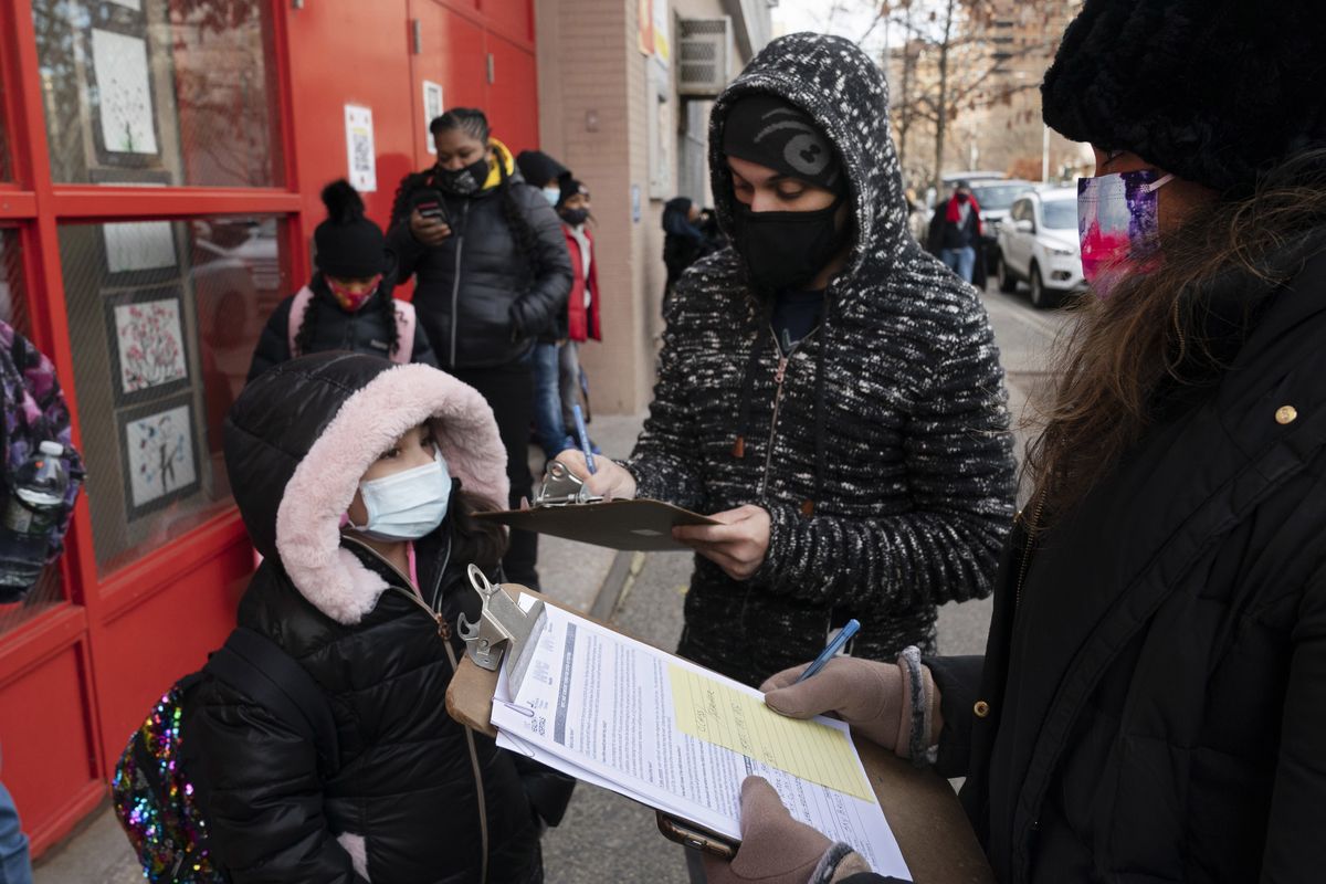 FILE - In this Dec. 7, 2020, file photo, a parent, center, completes a form granting permission for random COVID-19 testing for students as he arrives with his daughter, left, at P.S. 134 Henrietta Szold Elementary School, in New York. Children are having their noses swabbed or saliva sampled at school to test for the coronavirus in cities such as Baltimore, New York and Chicago. As more children return to school buildings this spring, widely varying approaches have emerged on how and whether to test students and staff members for the virus.   (Mark Lennihan)