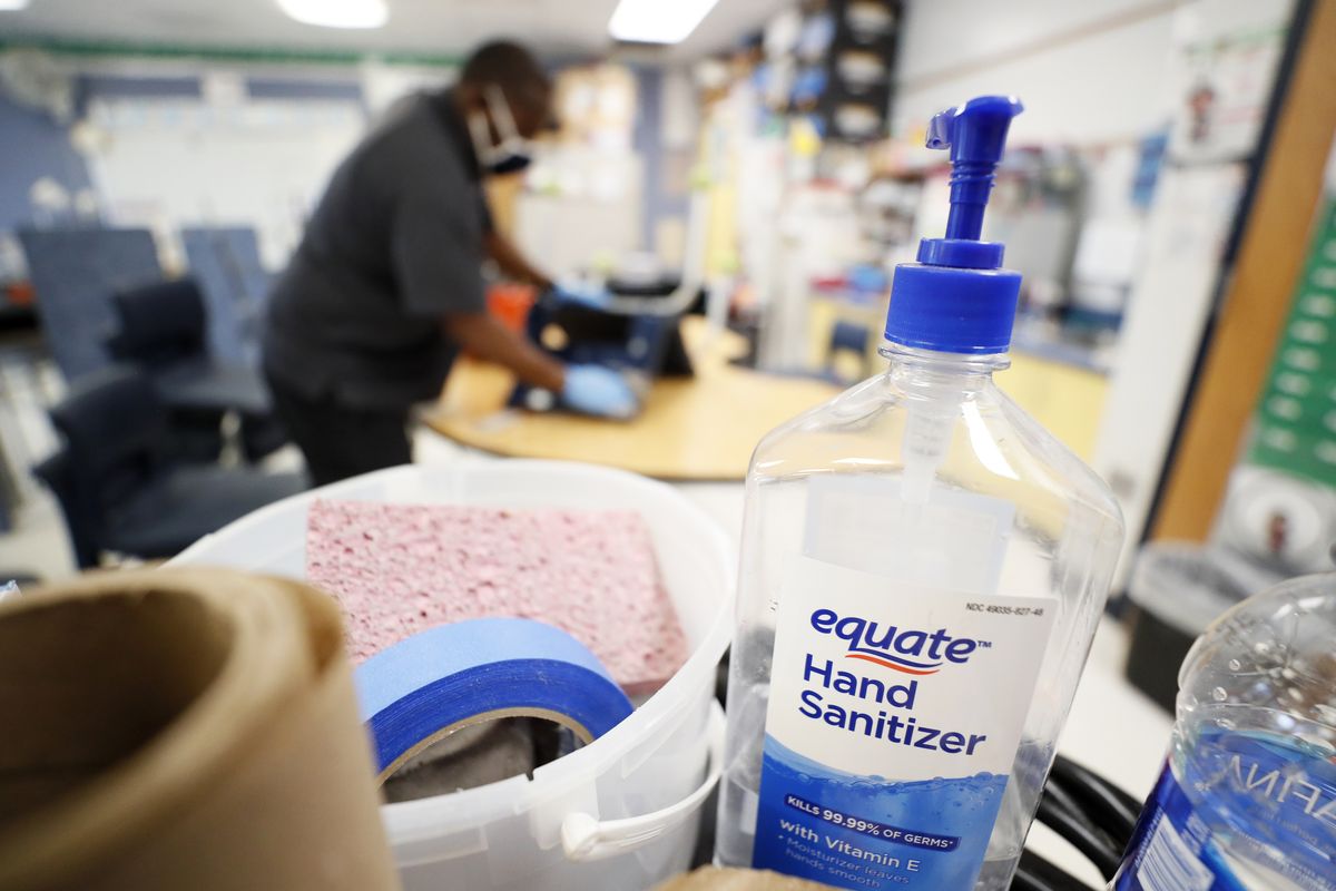 A bottle of hand sanitizer sits on a cart as Des Moines Public Schools custodian Tracy Harris cleans a chair in a classroom at Brubaker Elementary School, Wednesday, July 8, 2020, in Des Moines, Iowa. As the Trump administration pushes full steam ahead to force schools to resume in-person education, public health experts warn that a one-size-fits-all reopening could drive infection and death rates even higher.  (Charlie Neibergall)