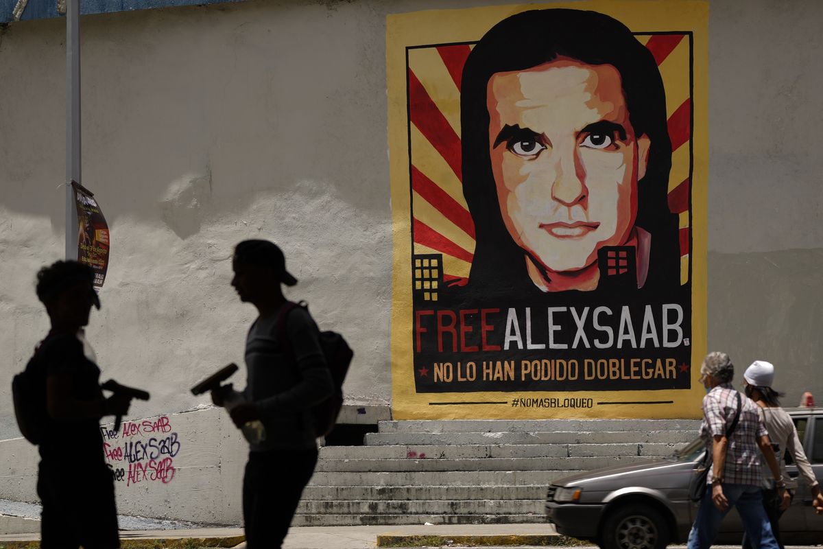 In this Sept. 9, 2021 photo, pedestrians walk near a poster asking for the freedom of Colombian businessman and Venezuelan special envoy Alex Saab, and that reads in Spanish "They haven
