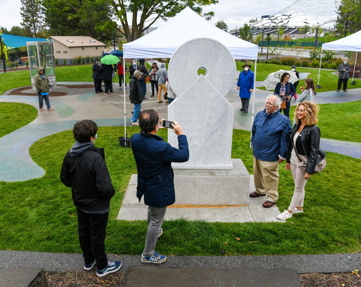 Maurizio Miozza snaps a picture of his wife, Elisabetta Valentini, Honorary Consul of Italy, Seattle, Wa., right, and John Caputo, President, Sister Cities Association of Spokane, moments before moving a dedication ceremony inside the U.S Pavilion for the monuments of Cagli, Italy (Teatro and Torrione), at center, and Spokane (Kokanee Steel), not seen, Saturday Sept. 18, 2021, in the Sister Cities Connections Garden in Riverfront Park.  (DAN PELLE/THE SPOKESMAN-REVIEW)