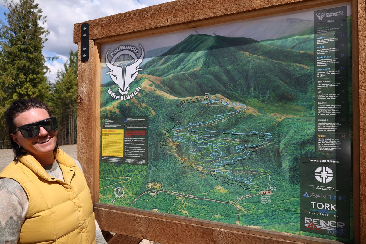 Jen Kalbach, owner of Panhandle Bike Ranch, stands next to the map of the 170-acre bike park on Monday near Sandpoint. The trail system has stirred discourse among local residents, with signs appearing along the road in support and opposition of the park.  (Mathew Callaghan / The Spokesman-Review)