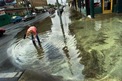 
Denise Shearer of The Globe wades into a puddle to unplug a storm sewer grate and get water draining off her sidewalk and out of the business on Friday. Thunder and lightning storms blew through Spokane in the late afternoon, bringing spot flooding to the area. 
 (Christopher Anderson / The Spokesman-Review)