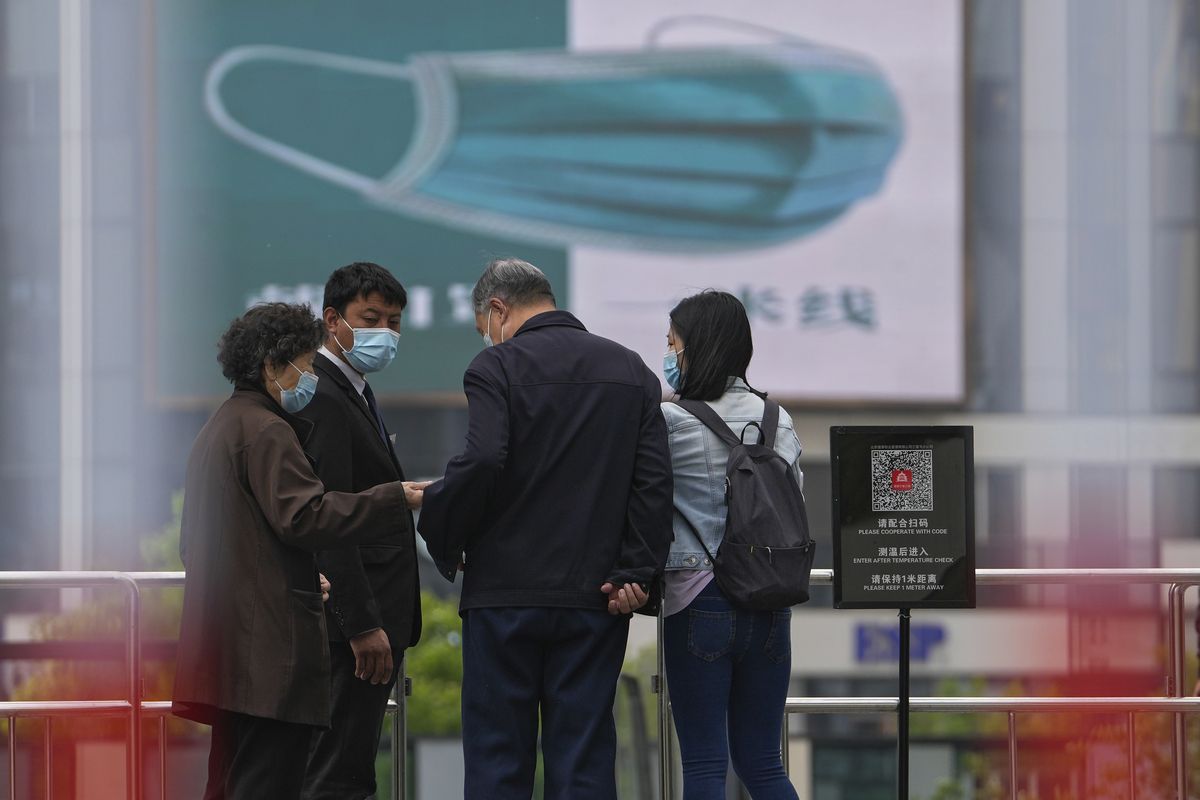 A security guard wearing a face mask stands watch as masked residents using their smartphone to scan their health code at a barricaded entrance to a commercial office complex, Sunday, April 24, 2022, in Beijing. Beijing is on alert after 10 middle school students tested positive for COVID-19, in what city officials said was an initial round of testing.  (Andy Wong)