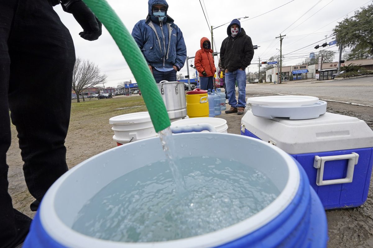 A water bucket is filled as others wait in near freezing temperatures to use a hose from public park spigot Thursday, Feb. 18, 2021, in Houston. Houston and several surrounding cities are under a boil water notice as many residents are still without running water in their homes.  (David J. Phillip)