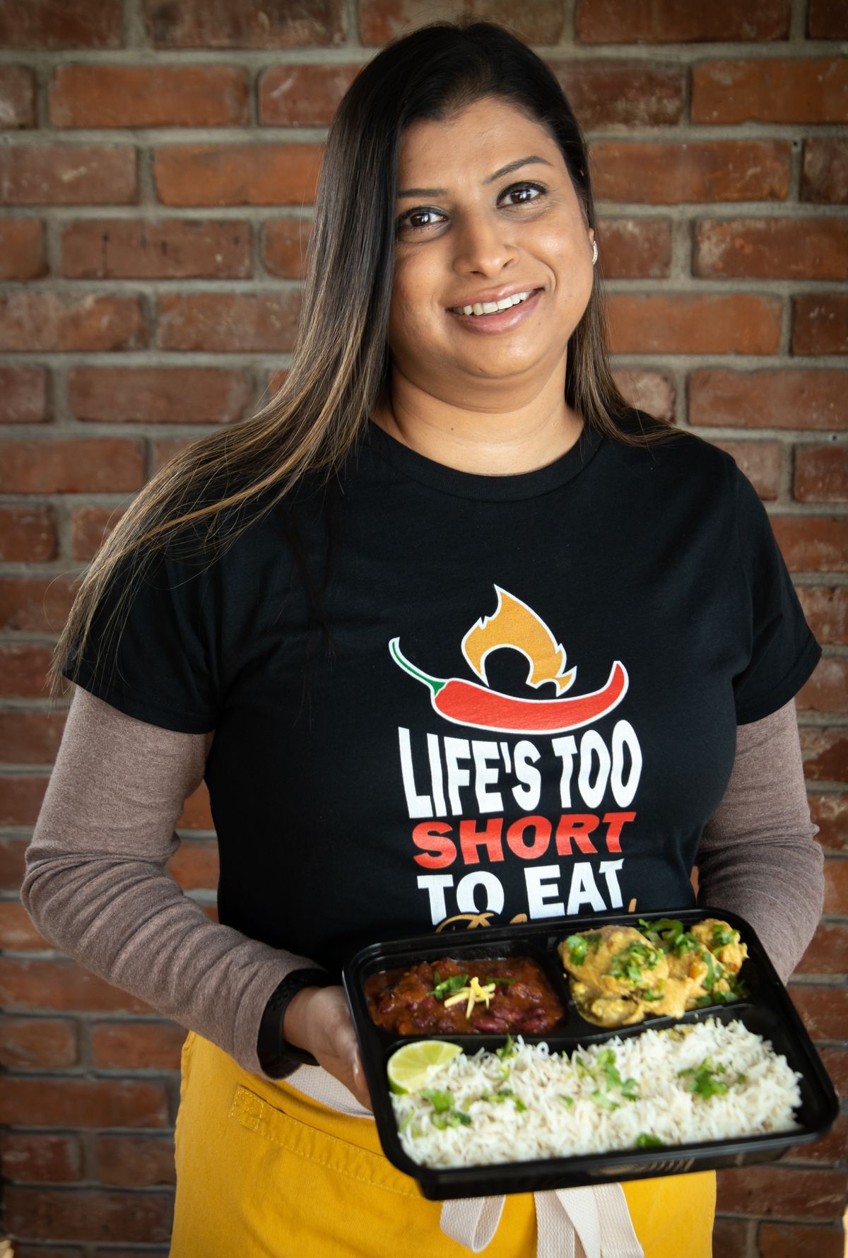 Noreen Hiskey, chef and owner of Inland Curry, holds a Punjabi meal that she made, comprised of cumin rice with Indian-style red beans and preserved lemon pepper chicken, at Feast World Kitchen on Sunday afternoon. Her T-shirt reads, “Life’s Too Short to Eat Bland Food.”  (Libby Kamrowski/The Spokesman-Review)