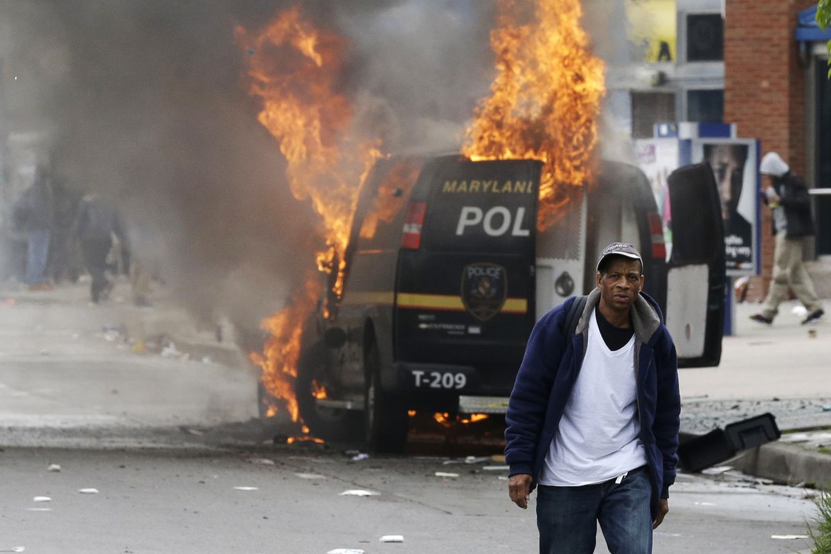 A man walks past a burning police vehicle Monday during unrest following the funeral of Freddie Gray in Baltimore. (Associated Press)
