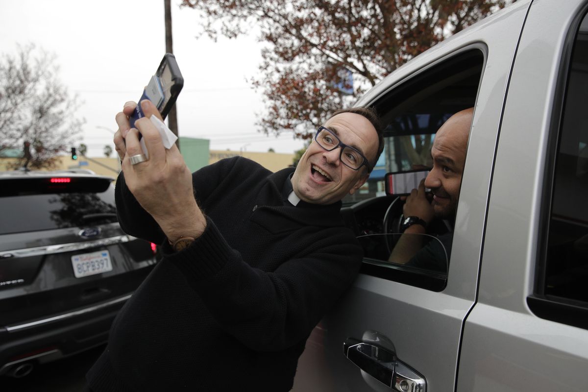 Father Jim Sichko, center, takes a selfie with a man Wednesday, Dec. 5, 2018, after paying for his lunch at an In-N-Out Burger in the Hollywood section of Los Angeles. “My approach is not so much speaking about the word of God, although I do a lot of that, but showing the presence of God through acts of kindness that kind of shock the individual and kind of cause them to, maybe cause them to. stop for a little bit,” he said. (Jae C. Hong / AP)