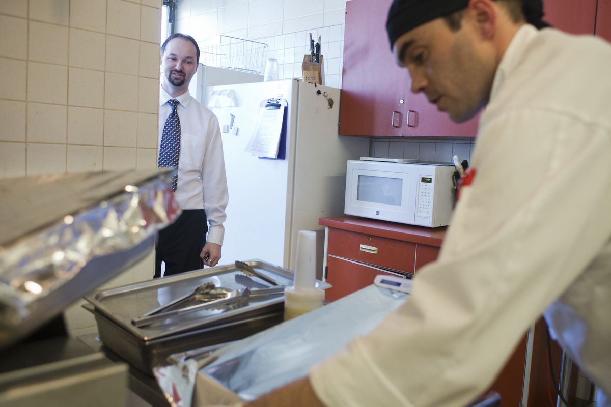 Landon Carrol, left, executive director of East Central Community Center, watches as Aron Larson, the new chef at the center, prepares hot food April 9. Larson’s hire means food is prepared at the center, and more people can be served with the same amount of money. (Jesse Tinsley)