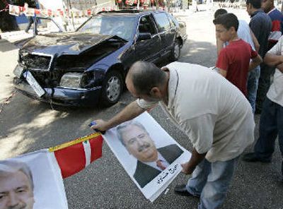 
A man hangs pictures of former Lebanese Communist Party chief George Hawi hours after he was killed by a bomb blast in his car, shown in background, in Beirut, Lebanon, on Tuesday. 
 (Associated Press / The Spokesman-Review)