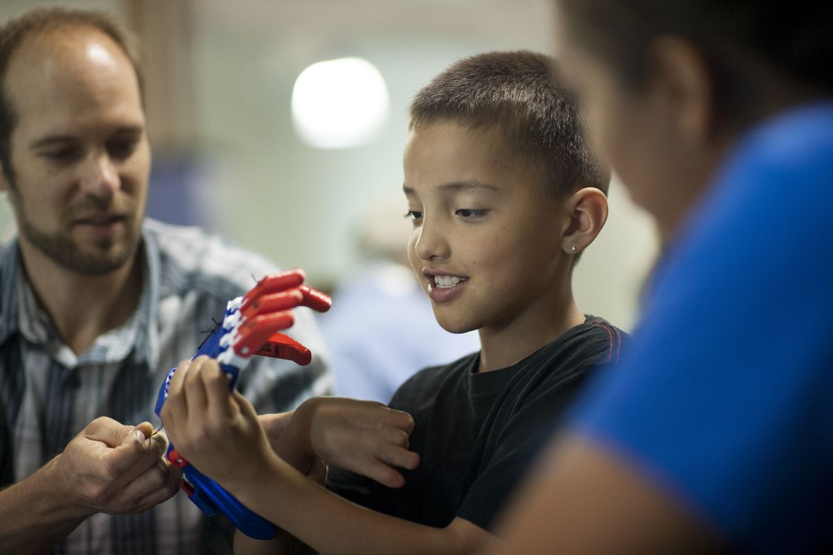 Marcus Lowley, 8, of Plummer, tries on his new prosthetic superhero hand with the help of Shriners Hospital’s Peter Springs, a certified prosthetist and orthotist, left, and Marcus’ mother Mandy Aripa, right, during an event that let children who are missing part or all of their hand create superhero prosthetic hands on Wednesday at Spokane Veterans Memorial Arena in Spokane. (Tyler Tjomsland)