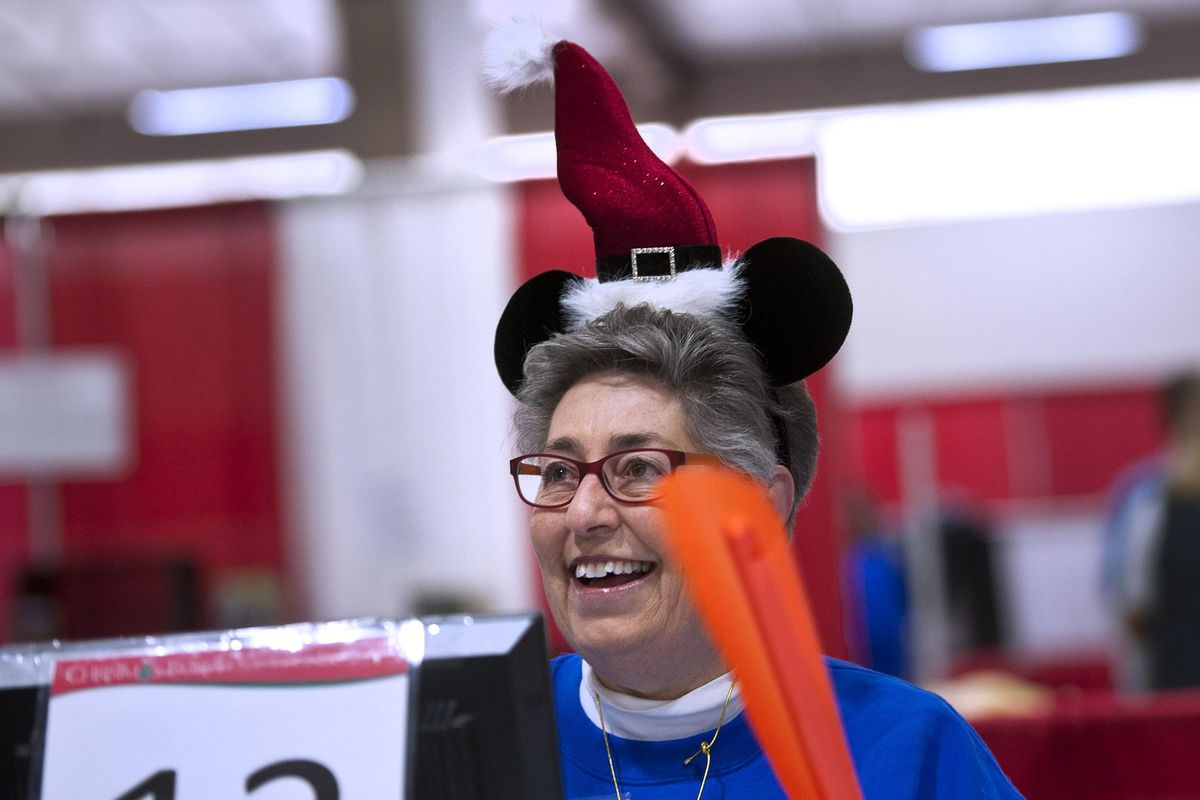 Volunteer Yvonne Shulman wears her Mickey Santa hat at the Christmas Bureau as she waves her flag to help the next person sign in on Monday, Dec. 18, 2017. (Kathy Plonka / The Spokesman-Review)