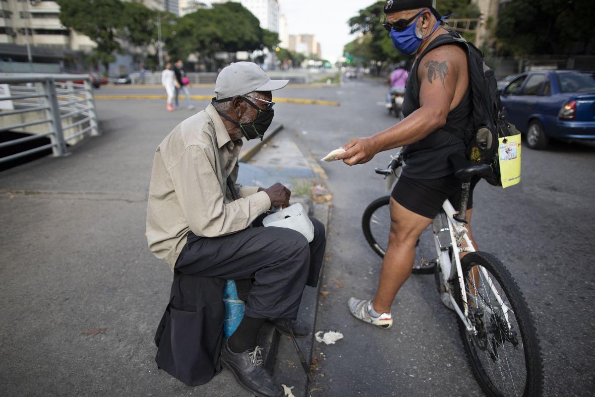 Andrés Burgos, a 55-year-old publicist, gives a package of arepas, or corn flour patties, Tuesday to a man begging for money at a traffic light in Caracas, Venezuela.  (Ariana Cubillos)