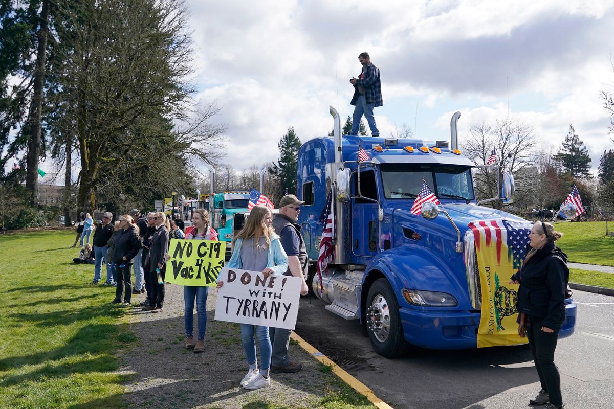 People hold signs as they stand near parked semi-trucks during a protest against COVID-19 vaccine mandates and other issues, Saturday, March 5, 2022, at the Capitol in Olympia, Wash. The trucks were part of a local convoy that traveled to Olympia for the protest.  (Ted S. Warren)