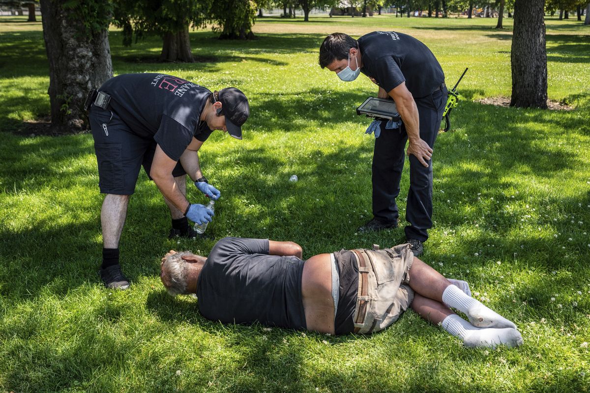 With temperatures well over 100 degrees on June 29, 2021,  Spokane firefighter Sean Condon, left and Lt. Gabe Mills, assigned to the Alternative Response Unit of of Station 1, check on the welfare of a man in Mission Park in Spokane.  (Colin Mulvany/The Spokesman-Review)