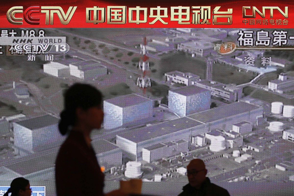 Hostess and delegate walk past a TV screen broadcasting Japan