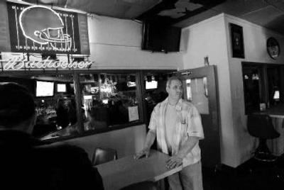 
Tavern owner Joe Myler, right, keeps a close eye on the front door of his bar Saturday. The tavern is split down the middle by a big glass wall, background. Myler added it along with a new ventilation system to create a separate room for smokers. Now, the $35,000 addition is essentially obsolete because of Ohio's ban on smoking inside most public places. 