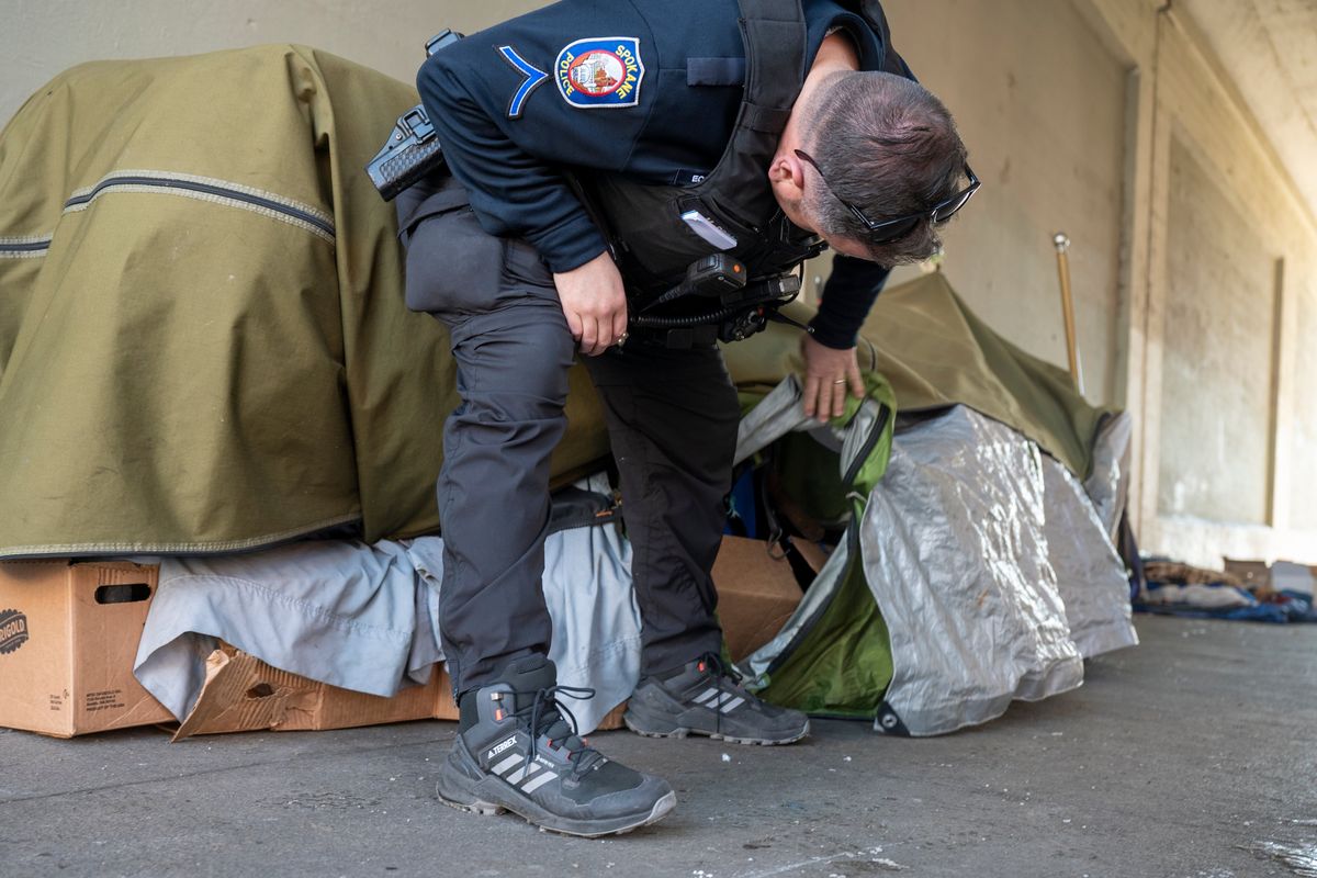 Spokane police Officer Micah Prim tries to ascertain if the resident of a tent-like structure is home on Friday in a tunnel under the train viaduct in downtown Spokane. The owner of the tent wasn’t present, and Prim made a note to come back and check on the owner.  (Jesse Tinsley/The Spokesman-Review)